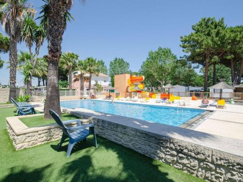 une piscine avec une chaise bleue à côté d'un palmier dans l'établissement Chalet near French Coast with Pool & Slide, au Grau-dʼAgde