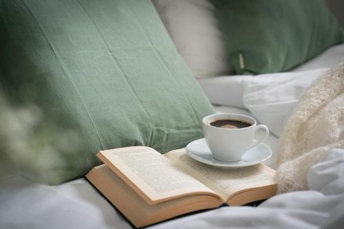 a cup of coffee and a book on a bed at Gamle Fengselet Kulturhotell in Stord