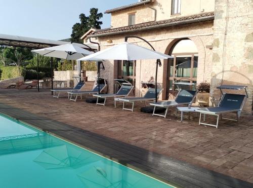 a pool with chairs and umbrellas next to a building at Corte Fratini Appartamenti in Trevi