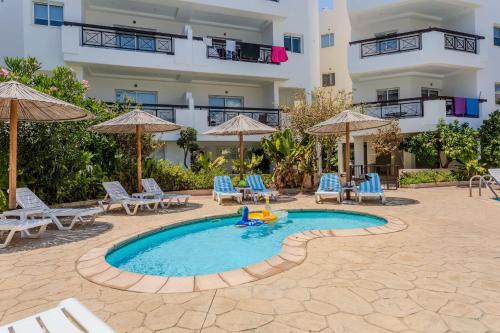 a swimming pool with chairs and umbrellas and a building at Artemis Cynthia Complex in Paphos City