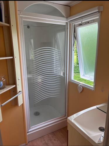La salle de bains est pourvue d'une douche en verre et d'une fenêtre. dans l'établissement Mobil-home au camping de bairon, à Le Chesne