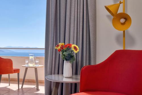 a living room with a red chair and a vase of flowers at Flisvos Royal Hotel & Suites in Tolo