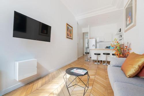 un salon avec un canapé et une télévision sur un mur dans l'établissement Luxe 1-BR Gem Louvre & Opera, à Paris