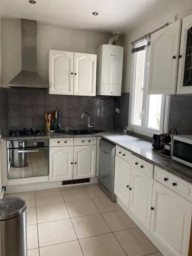 une cuisine avec des armoires blanches et des appareils en acier inoxydable dans l'établissement Charmante Maison Familiale près de Paris, à Drancy