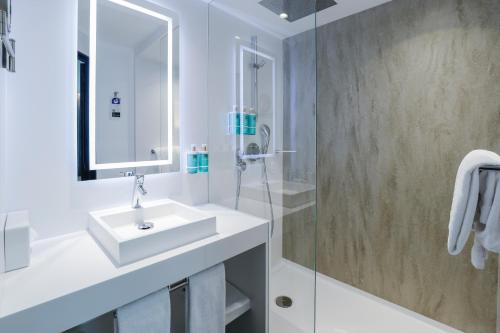 a white bathroom with a sink and a shower at Novotel Luxembourg Centre in Luxembourg