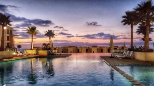 a pool at a resort with palm trees and a sunset at Appt magnifique vue mer et piscine spacieuse in Sidi Bouqnadel