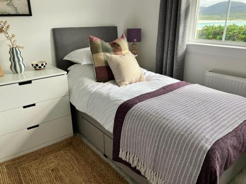 a bedroom with a bed with pillows and a window at Taigh Marsaili in Luskentyre