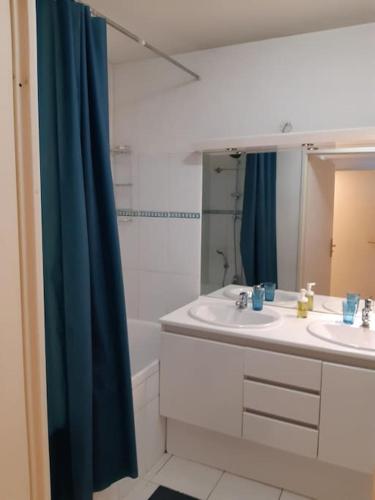 La salle de bains est pourvue de 2 lavabos et d'un rideau de douche bleu. dans l'établissement Spacieux logement Prado Rabateau idéal Famille, à Marseille