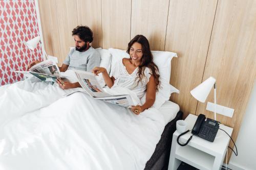 a man and a woman laying in bed reading newspapers at Stay Hotel Lisboa Aeroporto in Lisbon