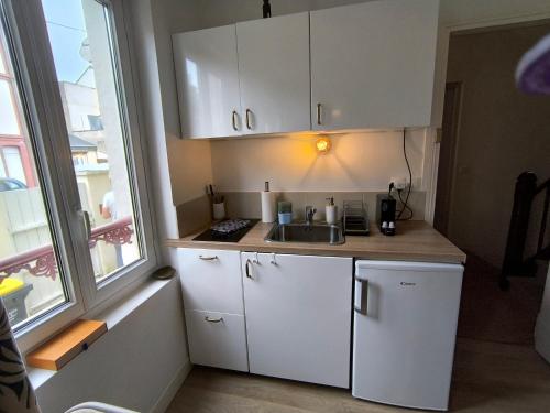une cuisine avec des armoires blanches, un évier et une fenêtre dans l'établissement Aux Planches souplex hyper-centre, à Deauville