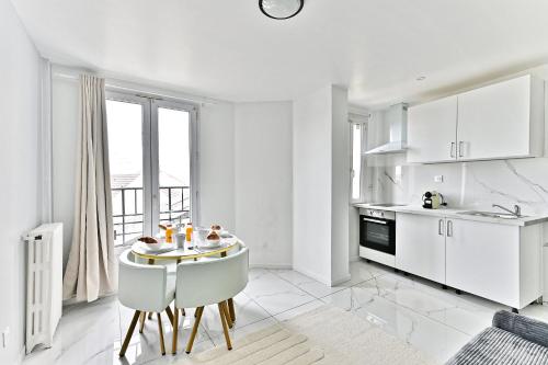 une cuisine avec des armoires blanches et une table et des chaises dans l'établissement Appartement Spacieux en banlieue parisienne - II, à Gagny
