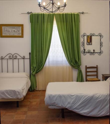 a bedroom with two beds and a window with green curtains at Cortijo del Coco in Fuente de Piedra