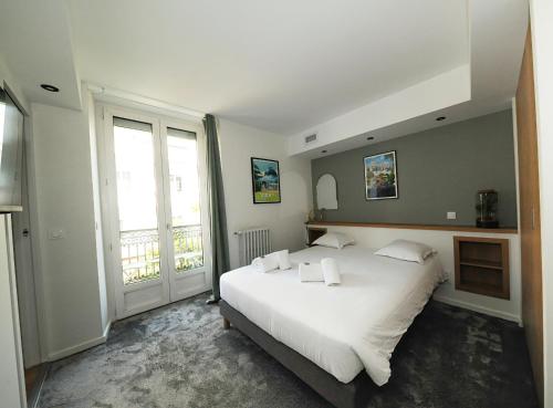 a bedroom with a large white bed and large windows at Hôtel & Restaurant Le Patio VICHY in Vichy