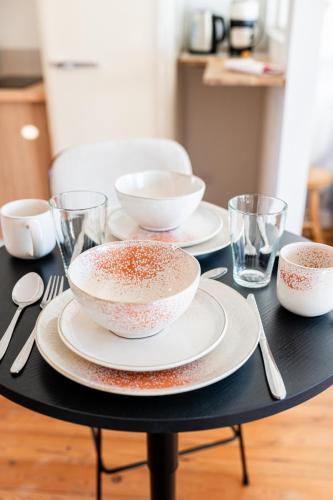 a black table with three bowls and plates and glasses at Villa Robs - Appartements tout confort, TV connectée, Haut débit, Localisation idéale - Courts séjours & Affaires in Caen