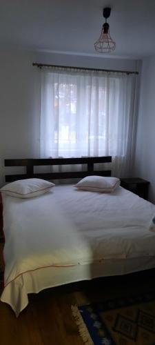 Un dormitorio con una gran cama blanca con ventana. en La Marginea Pădurii, en Marginea Pădurii