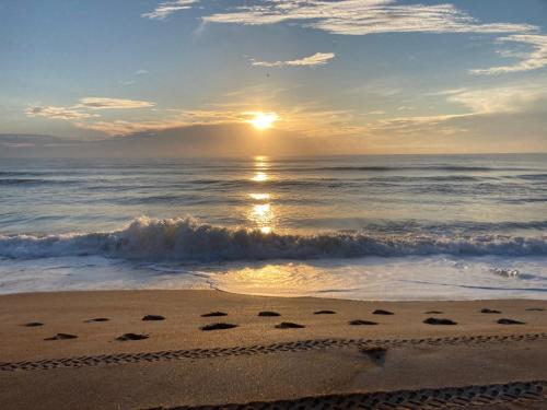 a sunset on the beach with footprints in the sand at Flamingo Heated Pool House in Palm Coast
