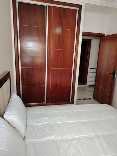 a bedroom with a white bed and wooden closet at lumineux, or et ébène Mariés et familles in El Jadida
