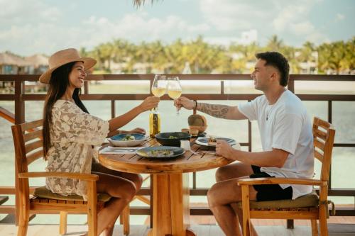 un hombre y una mujer sentados en una mesa con una copa de vino en Palafitos Overwater Bungalows, Catamarán, Cenote, All & More Inclusive - Adults Only, en Playa del Carmen