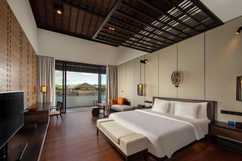 a bedroom with a large white bed and a living room at Radisson Blu Bali Uluwatu in Uluwatu