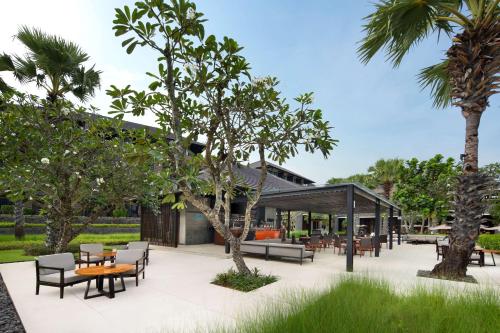 a patio with tables and chairs and palm trees at Radisson Blu Bali Uluwatu in Uluwatu
