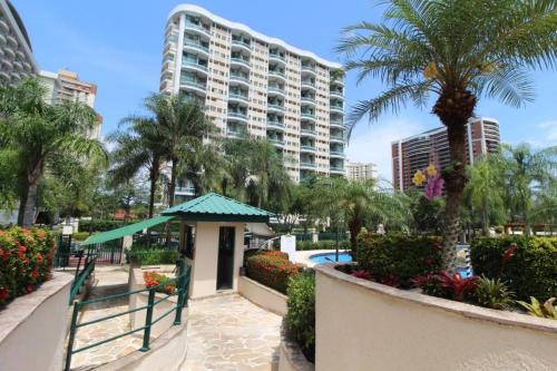 a resort with a pool and palm trees and a building at Barra da Tijuca - 508 - De Frente para Maravilhosa Piscina - Estacionamento Gratuito - Academia Comphania Atletica - Balsa para Praia Grátis - Microondas - Geladeira Grande - Recepção 24horas - Wi-Fi - Com Pia in Barra da Tijuca