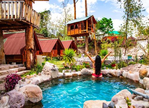 a girl sitting in a pool of water with a tree house at El Huayllar in Cusco