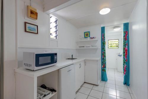 a kitchen with white cabinets and a microwave at Vaka Beach Cottage with AC Unlimited Wifi in Rarotonga