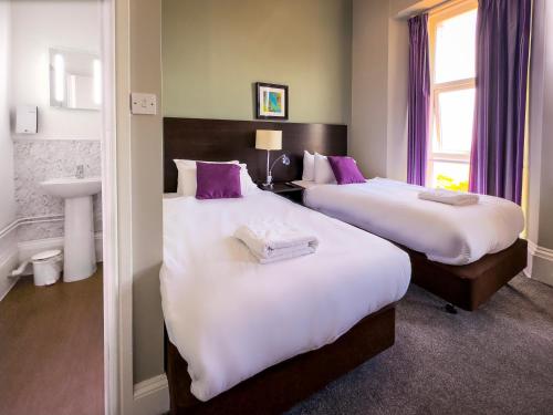 two beds in a hotel room with purple pillows at The Esplanade Hotel by Compass Hospitality in Paignton