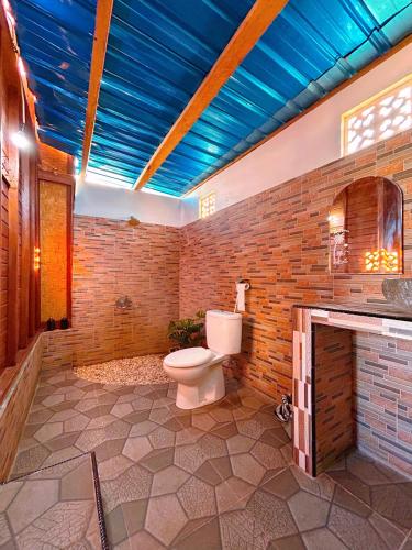 a bathroom with a toilet and a brick wall at Batur cottage in Kubupenlokan