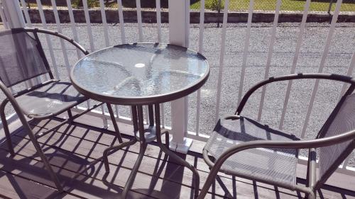 a glass table and two chairs on a balcony at Petit Hôtel Amara in La Malbaie