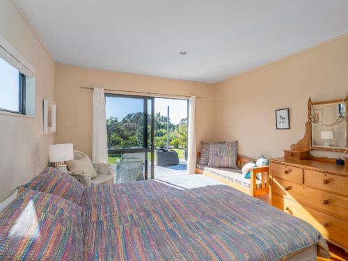 a bedroom with a large bed and a sliding glass door at Wai Whare - Kūaotunu Holiday Home in Whitianga