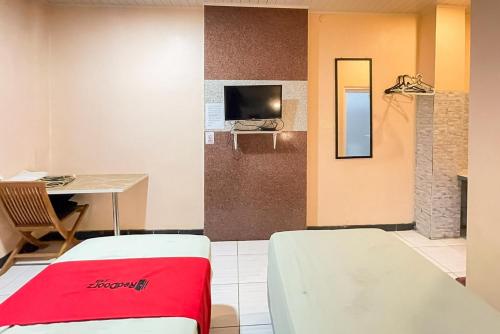 a room with two beds and a table and a tv at RedDoorz Syariah near Mall Of Serang in Kumprung