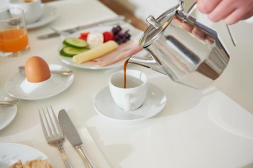 a person pouring coffee into a cup on a table with food at Kapellerhof in Stadl-Paura