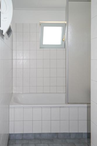 a white tiled bathroom with a tub and a window at Dike House Affordable 6-Person Holiday Home Near the Sea Dike in Anjum