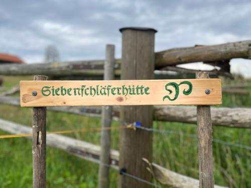 a wooden sign on a wooden fence with a pasture at Siebenschläferhütte in Buchenberg