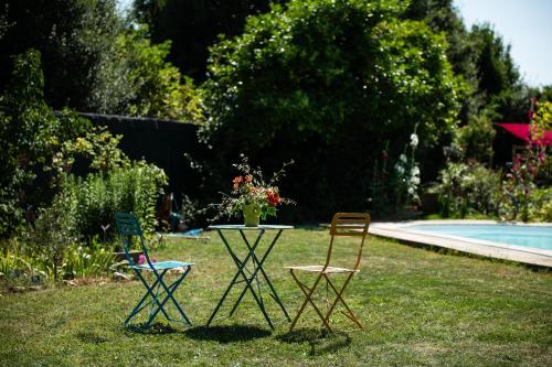 two chairs and a table in the grass near a pool at La Jolie Longère Fleurie Lodge avec piscine et jardin in Le Gué-dʼAlléré