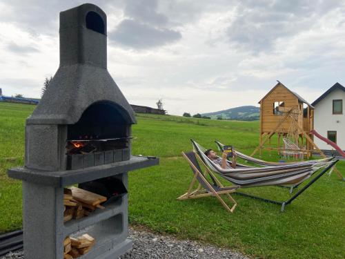 a man sitting in a hammock next to a pizza oven at Jagodowe Domki in Ciche