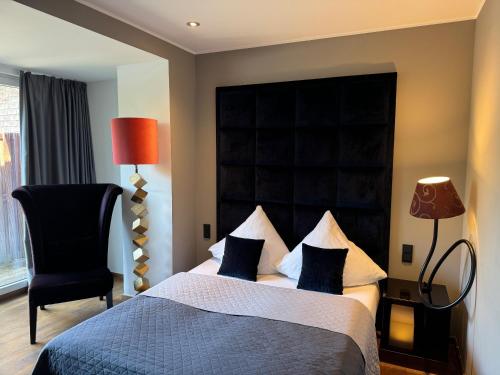 a bedroom with a bed with a black headboard and a chair at Hotel Rosenmeer in Mönchengladbach