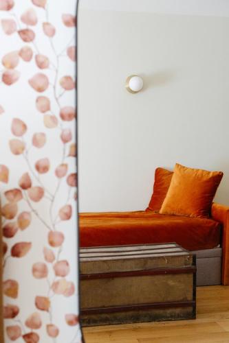a bed with an orange pillow and a curtain at Hôtel Le Mouton Bleu in Talloires