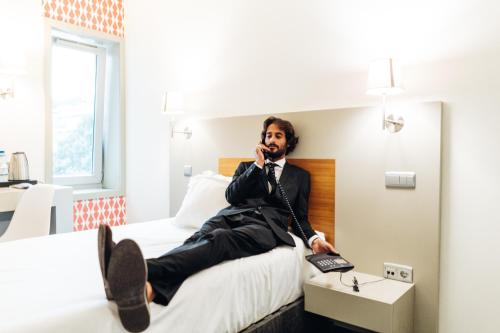 a man sitting on a bed talking on a cell phone at Stay Hotel Guimarães Centro in Guimarães