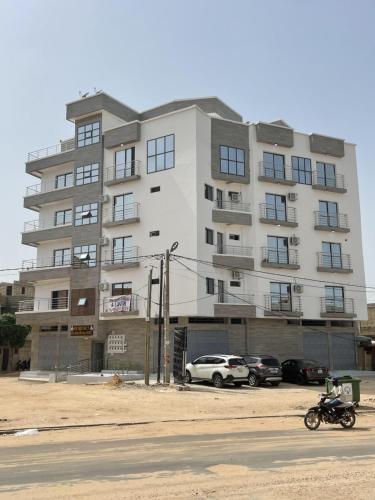 a large white building with cars parked in front of it at Résidence Cheikh Mahy Cisse Appartements, studios et chambres a louer meublé et climatisé in Kaolack