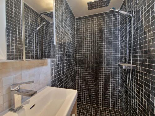 La salle de bains est pourvue de carrelage noir, d'un lavabo et d'une douche. dans l'établissement Havre de paix aux Batignolles, à Paris