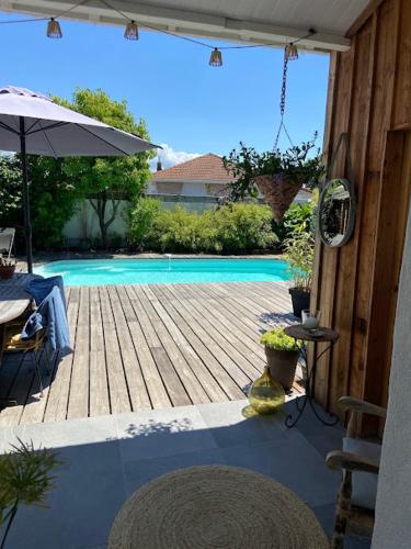 une terrasse avec une piscine, une table et un parasol dans l'établissement Maison de charme familiale Bassin Arcachon, à La Teste-de-Buch