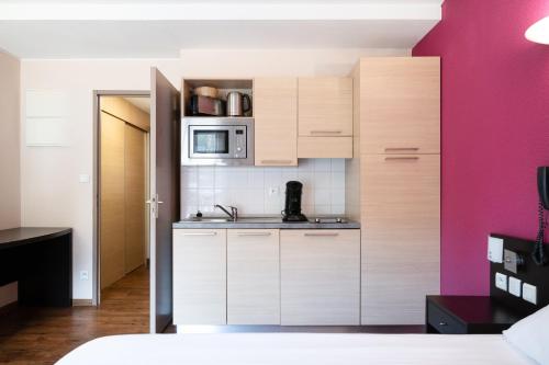a kitchen with white cabinets and a pink wall at Résidence Le Grand Tétras- SPA THERMAL INCLUS in Ax-les-Thermes