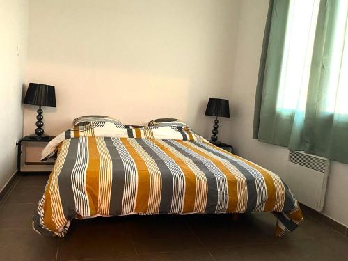 - une chambre avec un lit avec une couette rayée et 2 lampes dans l'établissement Charmant T2 calme centre ville, à La Crau