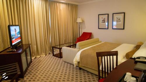 a hotel room with a bed and a couch and a television at Phakalane Golf Estate Hotel & Convention Centre in Gaborone