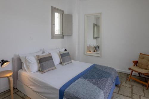 a bedroom with a white bed with pillows and a chair at By The Stone Tinos in Triandáros