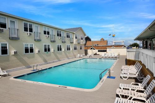 a swimming pool with white chairs and a building at Grove Hotel in Cherry Grove