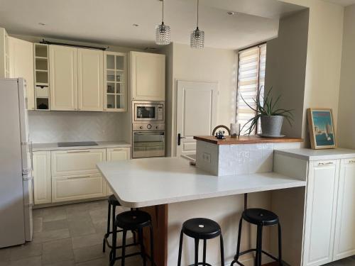 une cuisine avec des armoires blanches et un comptoir avec des tabourets dans l'établissement Maison de ville à deux pas de la dune du Pilat, à Salles
