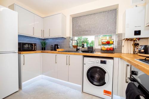 a kitchen with white cabinets and a washer and dryer at Stylish 2-Bed Flat on Banbury Road in Oxford